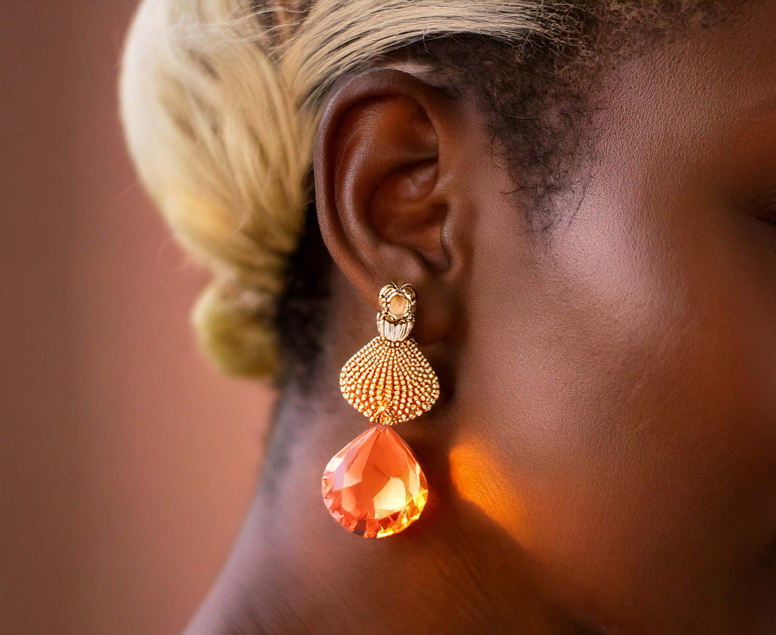 Gros plan d’une oreille avec une boucle d’oreille orange reflétant la lumière.